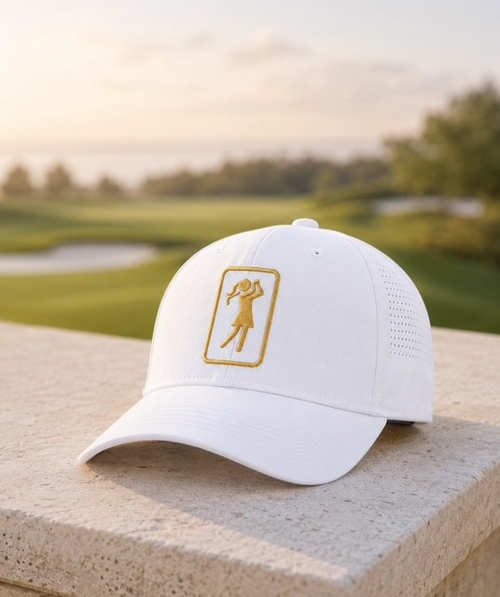 Aurora Dawn golf hat with gold logo resting on a stone ledge overlooking the golf course at sunrise
