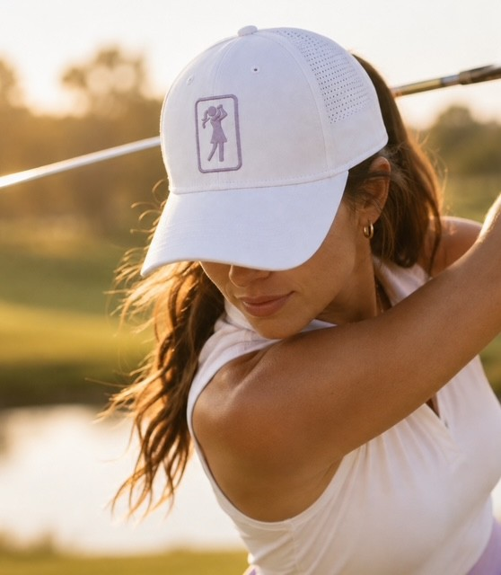 Woman mid-swing wearing the Heather golf hat on the course at golden hour